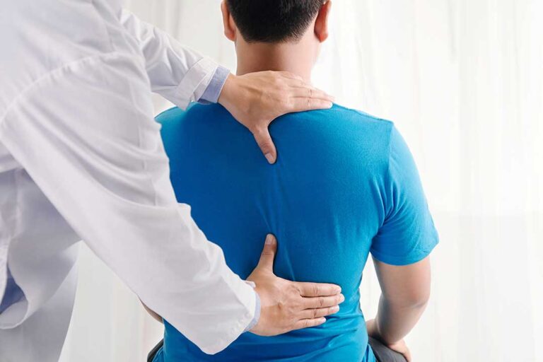 Person gently stretching a sore lower back beside a living room chair.