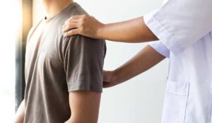 Person discussing shoulder and back pain with a clinician during a seated musculoskeletal assessment.