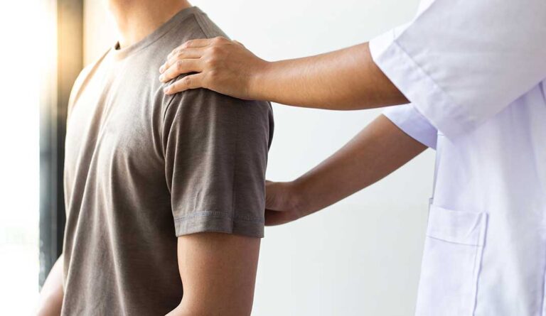 Person discussing shoulder and back pain with a clinician during a seated musculoskeletal assessment.